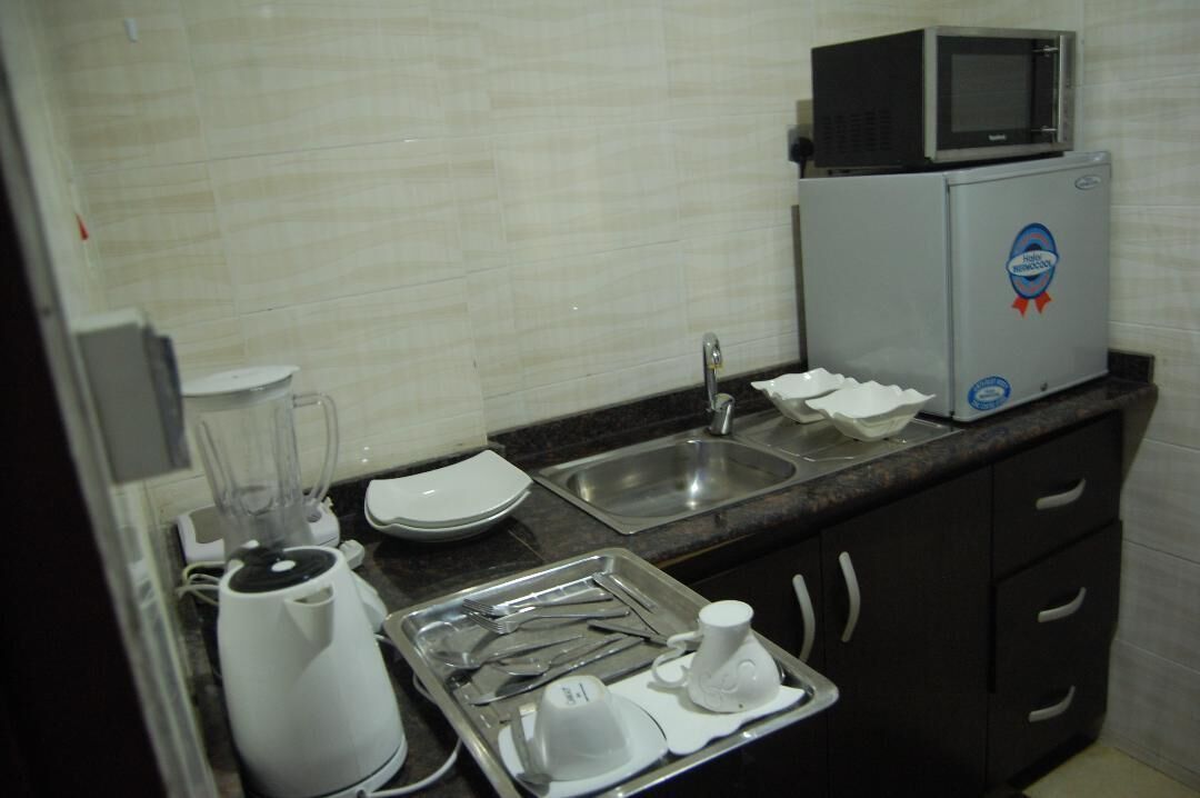 A kitchenette with a microwave, toaster, blender, sink, and a tray with utensils.