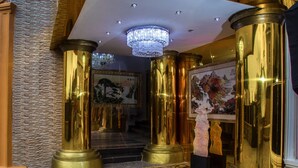 Un lobby imponente con pilares dorados decorados, un candelabro y arte clásico.