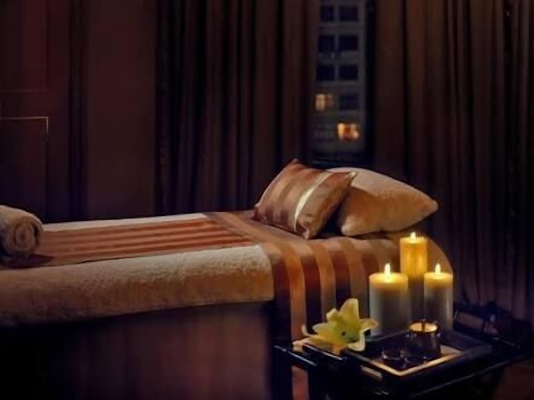 A dimly lit room with a bed, a nightstand with candles, and a window with curtains.