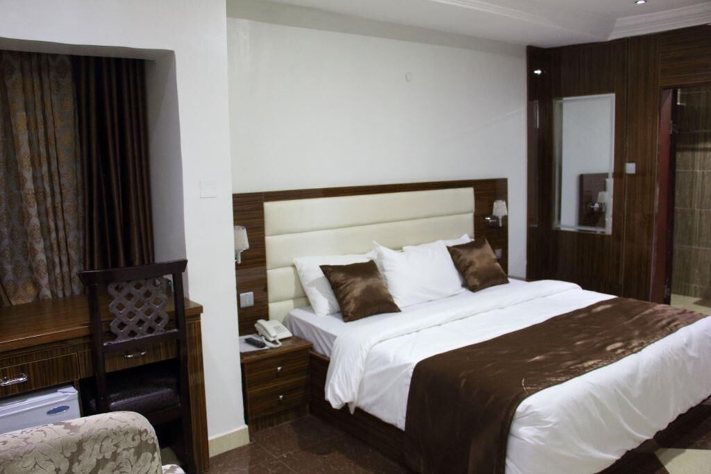 A hotel room with a large bed, a wooden nightstand, a telephone, and a mirror.