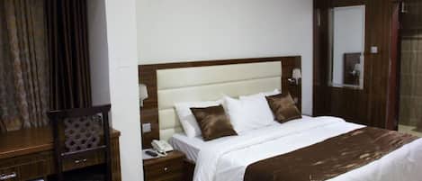Habitación de hotel con una cama grande, una mesita de noche de madera, un teléfono y un espejo.