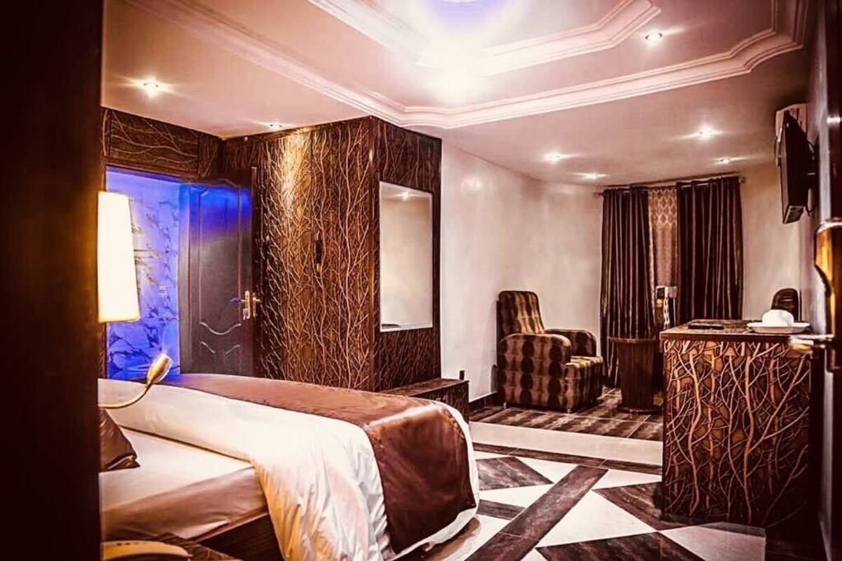 A hotel room with a bed, a chair, a desk, and a bathroom with a mirror.