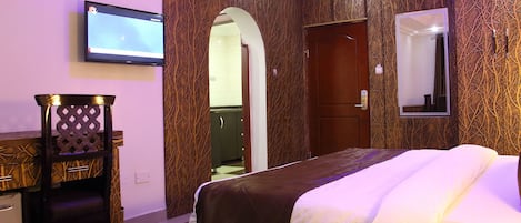 A hotel room with a bed, a TV mounted on the wall, a wooden chair, and a wardrobe.