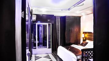 Habitación de hotel con cama, vestidor y baño con cabina de ducha de vidrio.