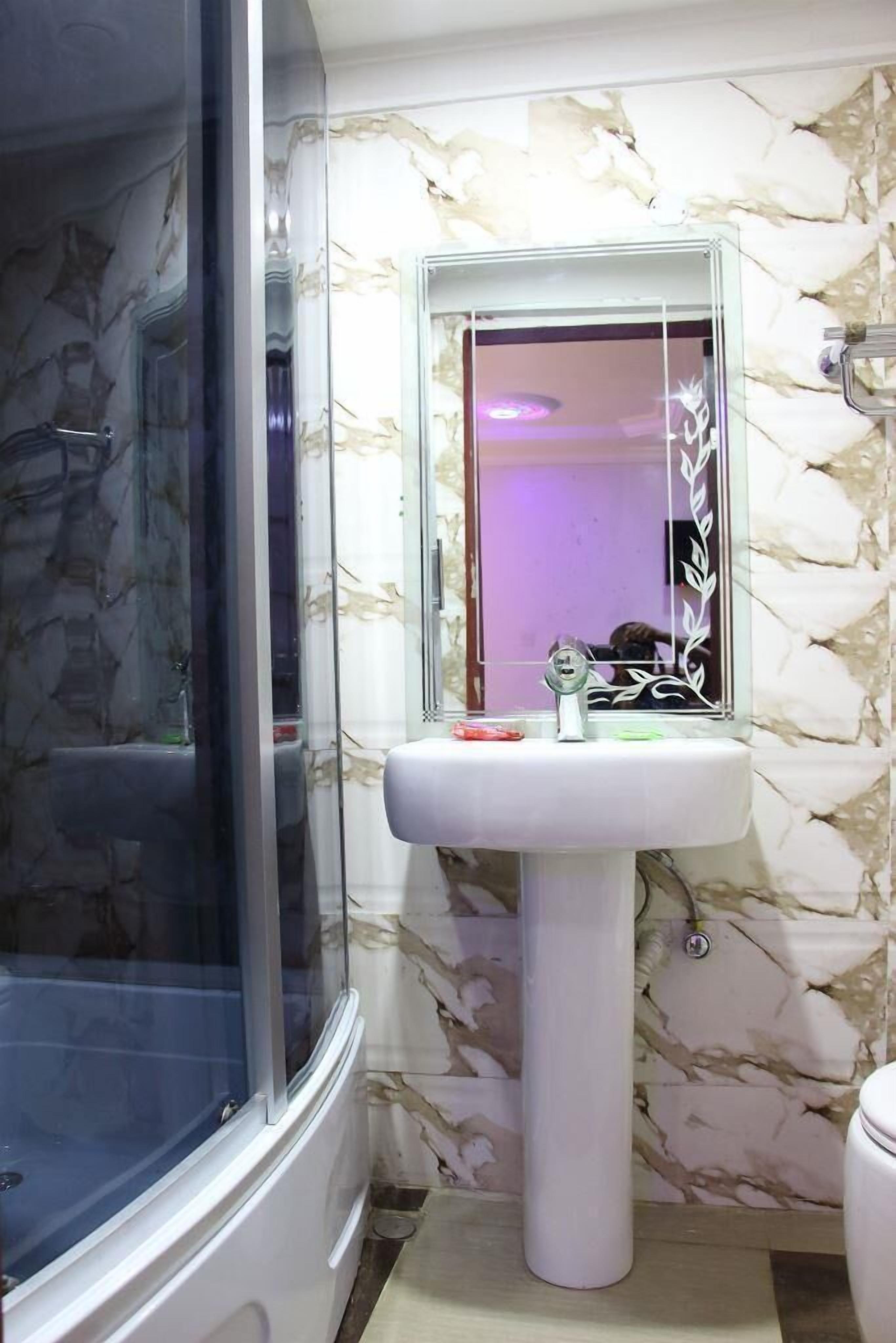A bathroom with a marble-patterned wall, a pedestal sink, and a glass-enclosed shower.