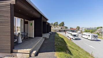 A modern building with a covered outdoor seating area, a road with RVs, and a clear sky.