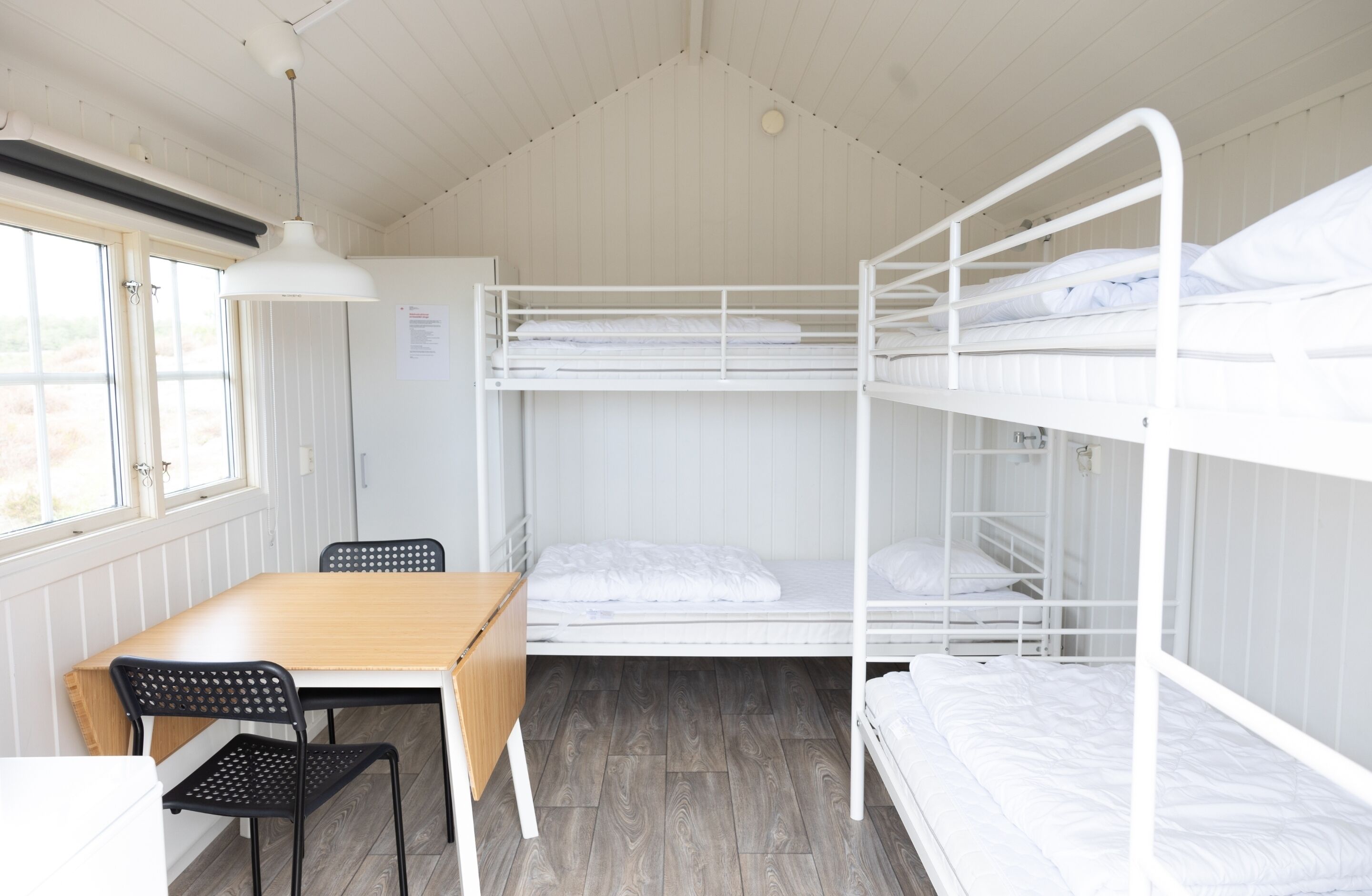 Et soveværelse med køjeseng, et træbord og stole, et vindue og et hvidt loft.