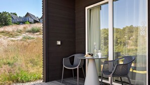 A balcony with two chairs and a table, overlooking a grassy area and a building in the background. - First Camp City Strömstad (Stromstad)