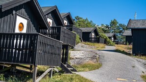 A row of wooden cabins with balconies, a gravel path leading through them, and a clear blue sky. - First Camp City Strömstad (Stromstad)