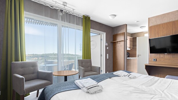 A hotel room with a large bed, two armchairs, a small table, a TV, and a sliding door to the balcony. - First Camp City Strömstad (Stromstad)