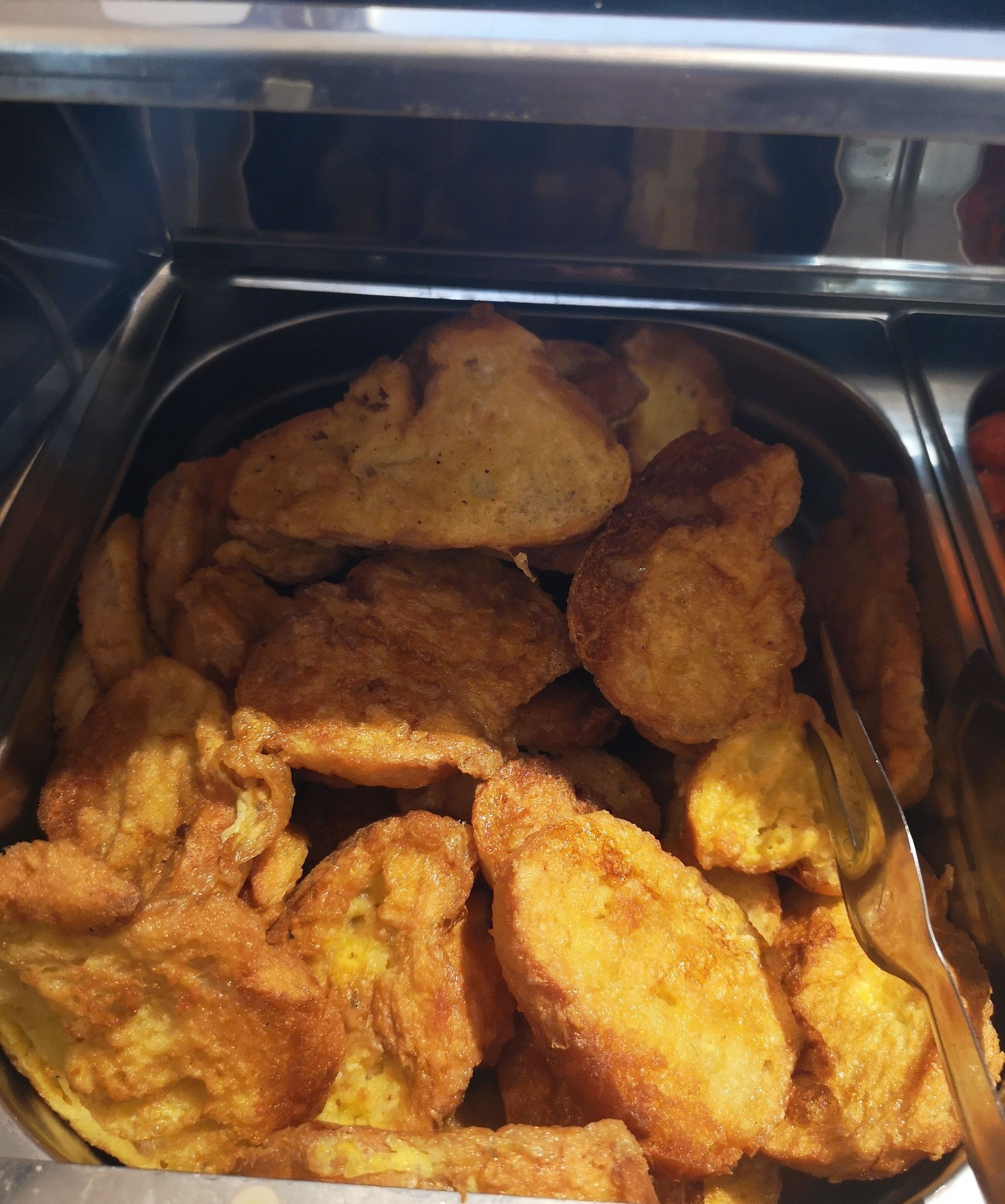 A tray of fried food items, likely fritters or similar snacks, in a metal container.