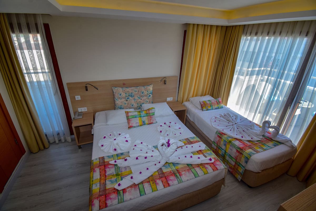 A hotel room with two beds, each with a colorful bedspread and white towels arranged in a bow shape.