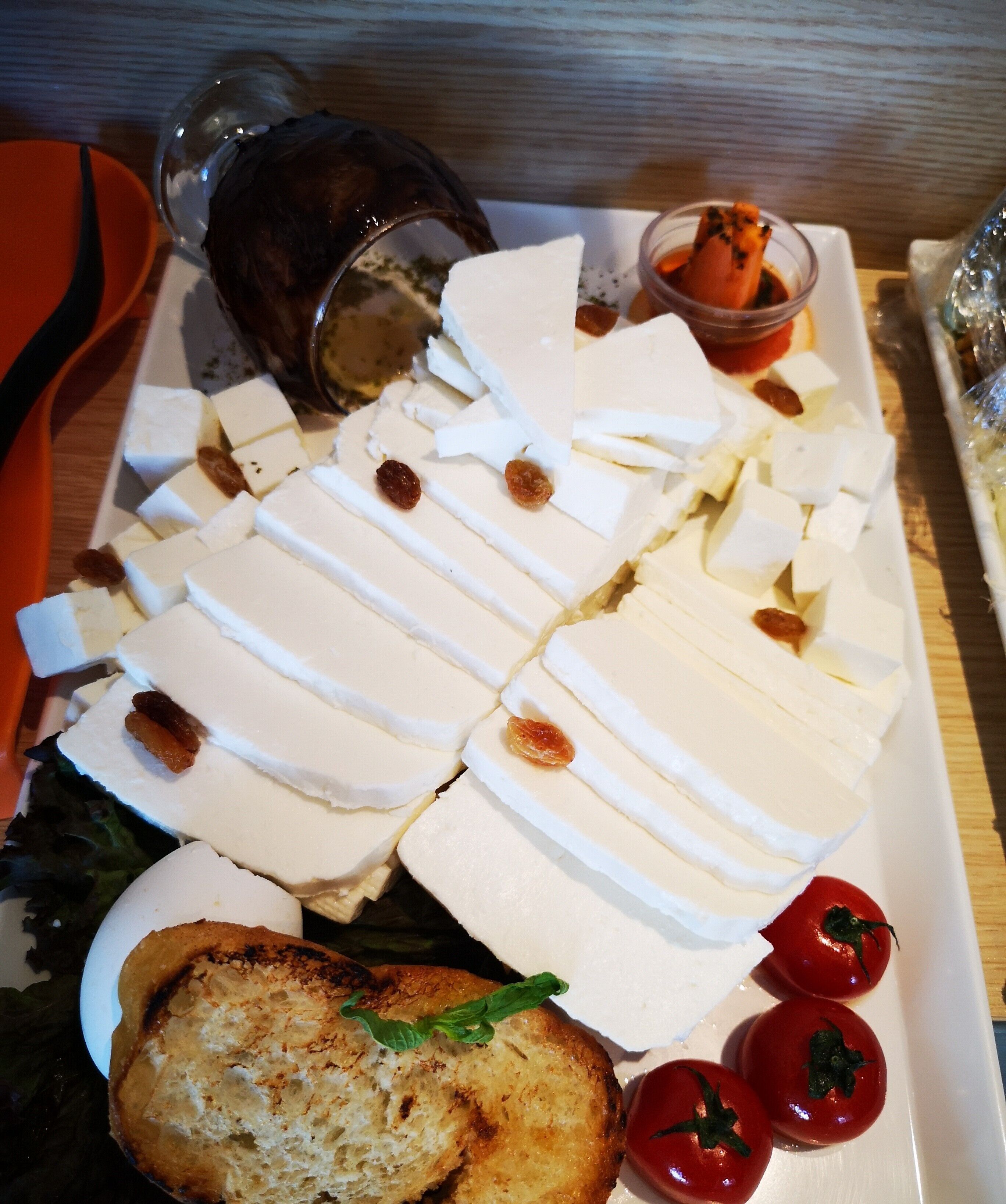 Une assiette de fromage coupé en tranches, accompagnée de tomates et de pain.
