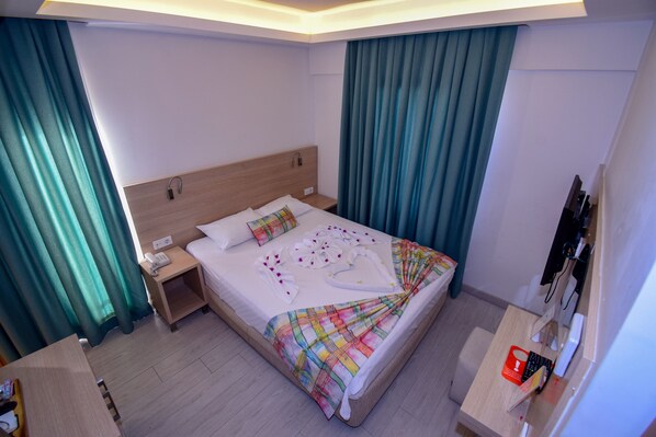 A hotel room with a bed, a bedside table with a phone, a desk with a computer, and a TV.