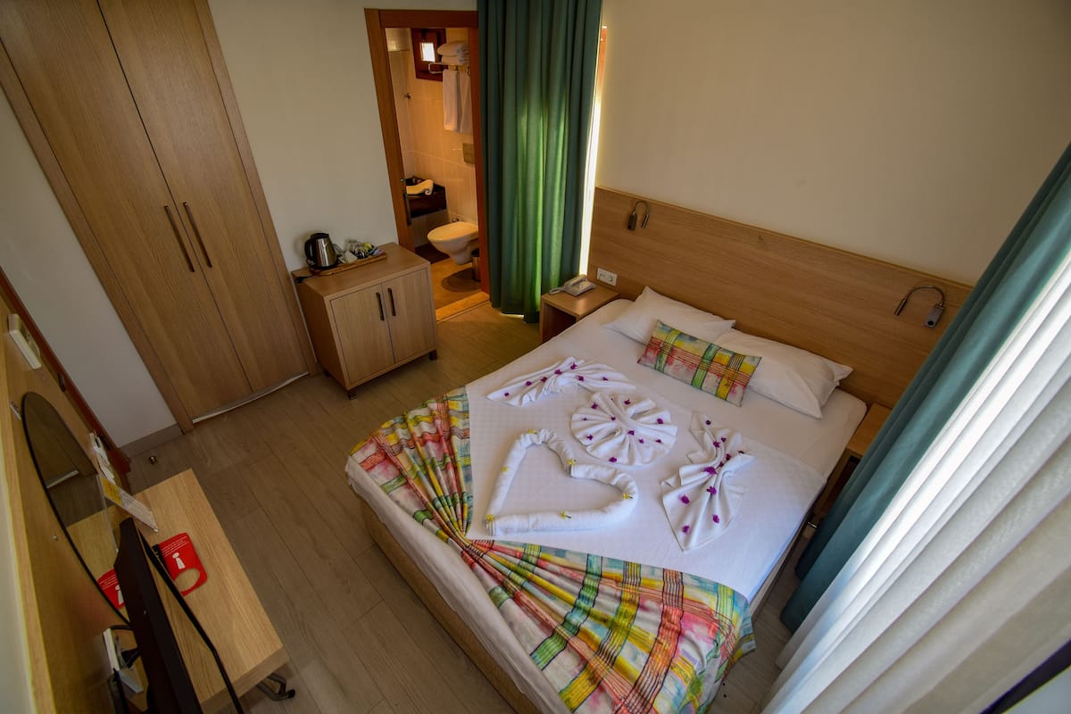 A hotel room with a bed, a wooden wardrobe, a bathroom, and a desk with a telephone.