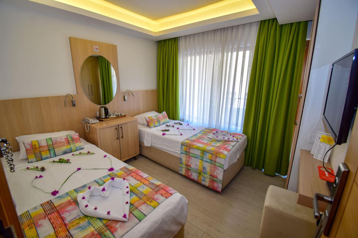 A hotel room with two beds, a wooden headboard, a mirror, a television, and a desk with a chair.