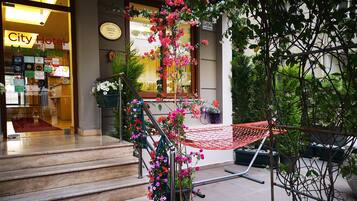 A hotel entrance with a staircase leading to a covered area, a hammock, and a variety of plants.