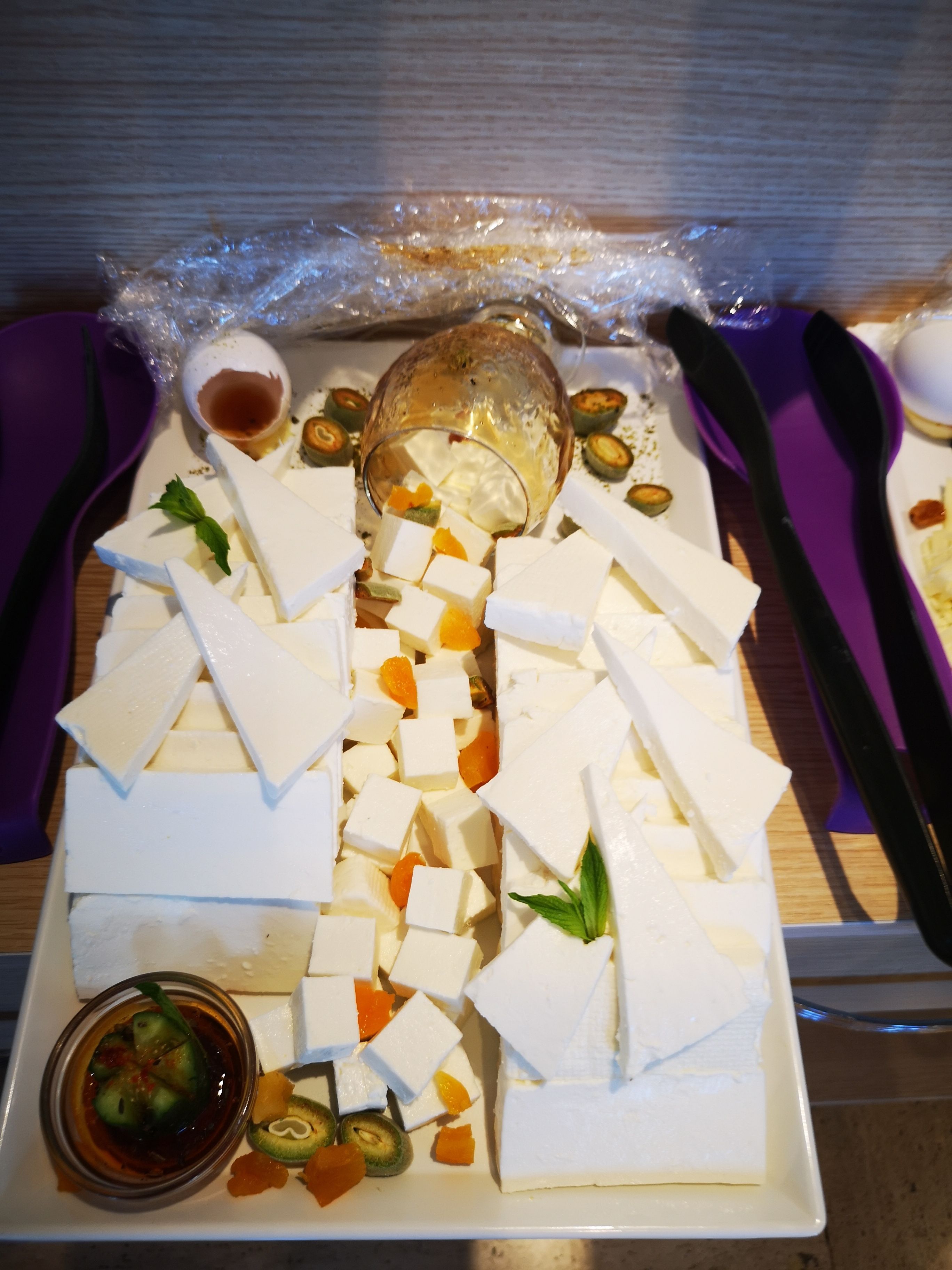 Une planche de fromages avec différents types de fromages, des noix et un petit bol de sauce.
