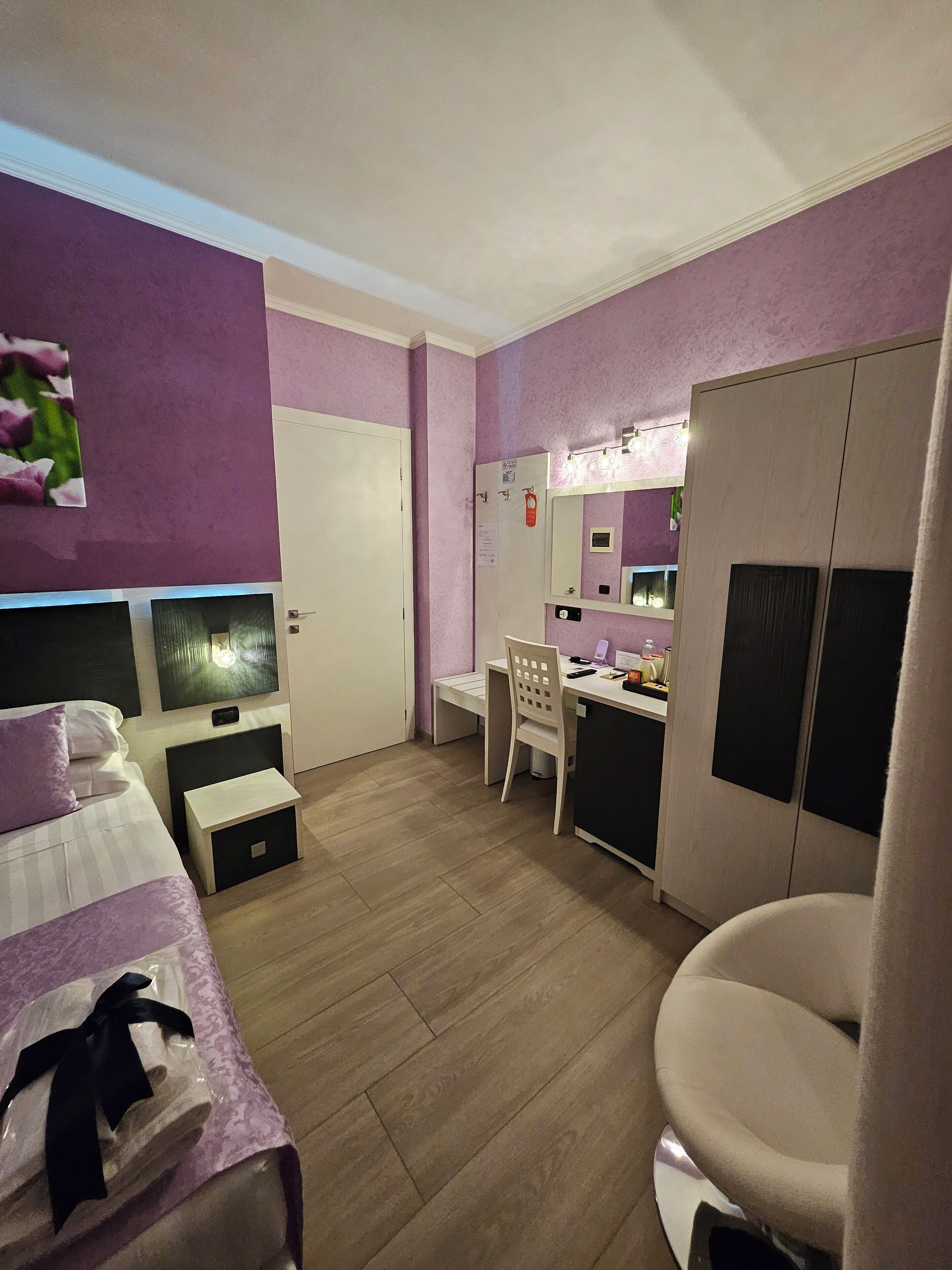 A bedroom with a bed, bedside table, and a desk with a chair. There is a wardrobe and a mirror on the wall.