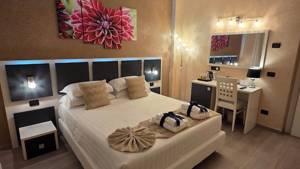 Een hotelkamer met een groot bed, nachtkastjes, een bureau, een spiegel en een bloemrijk kunstwerk aan de muur.