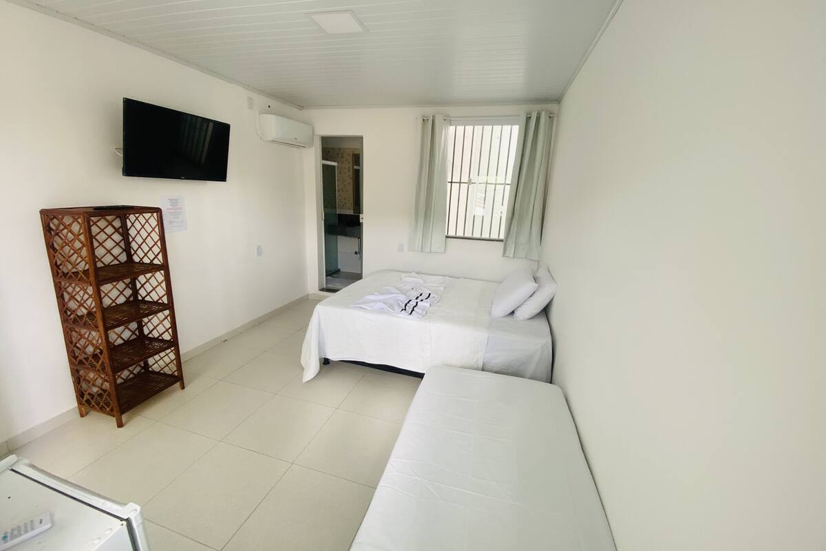 Ein Schlafzimmer mit einem Bett, einem an der Wand montierten Fernseher, einem Holzregal und einem Fenster mit Vorhängen.