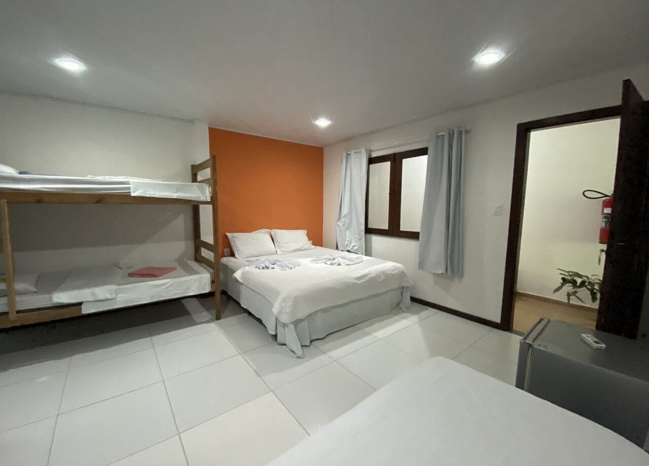 A bedroom with bunk beds, a single bed, a desk, and a window with curtains.