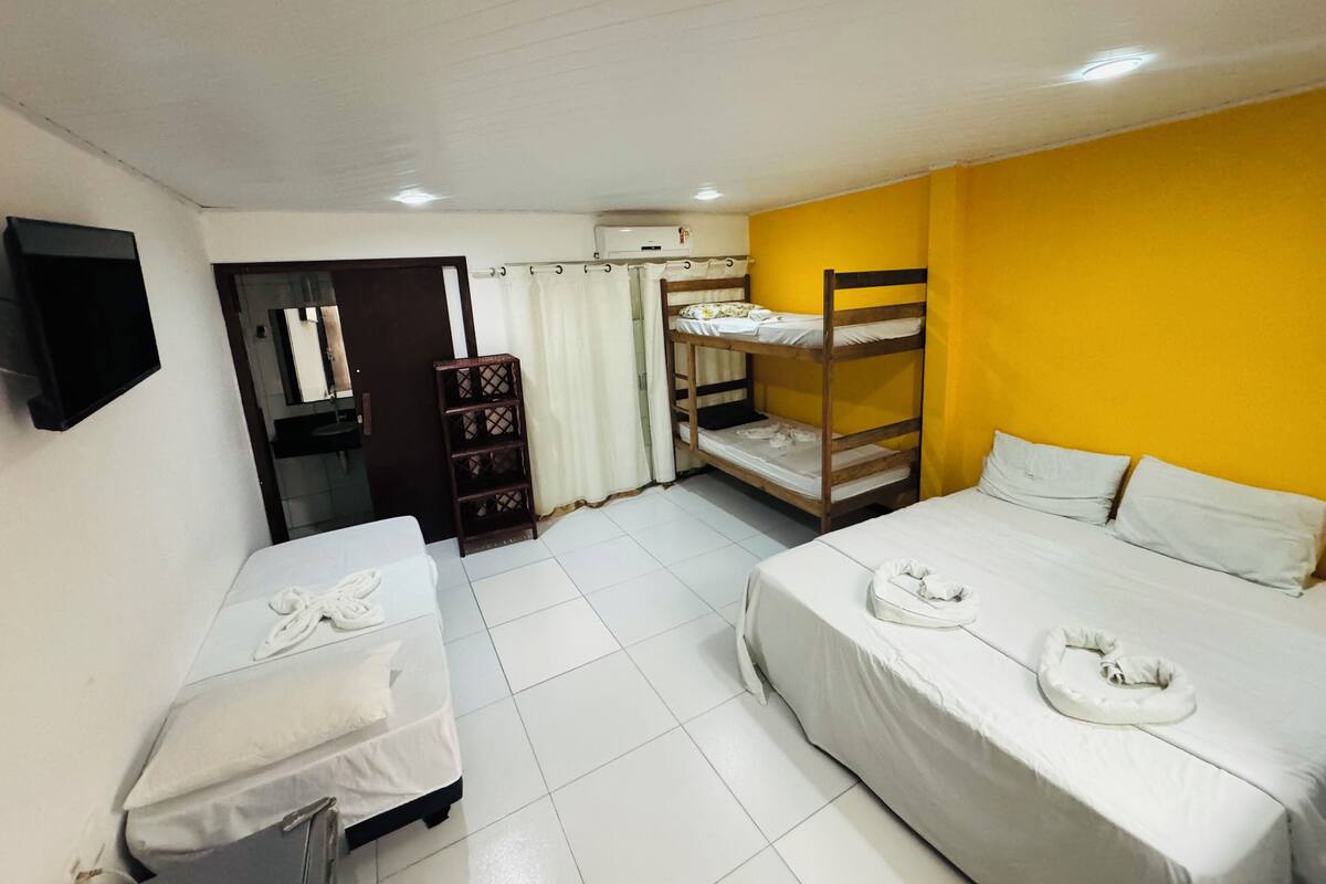 Ein Hotelzimmer mit zwei Einzelbetten, einem Etagenbett, einem Fernseher, einem Kleiderschrank und einem Badezimmer mit Spiegel und Toilette.