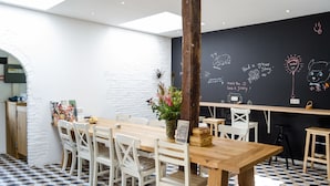 A dining area with a wooden table and white chairs, a blackboard with drawings and text, and a checkered floor pattern.
