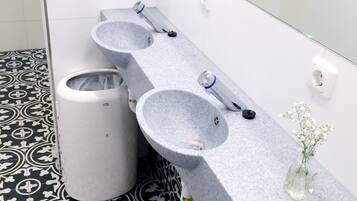 A bathroom with three sinks, a trash bin, and a vase with flowers.
