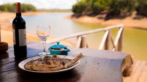 A wooden table with a plate of grilled fish, a wine bottle, and a glass of wine. - Le Chateau du Lac (Mantasoa)