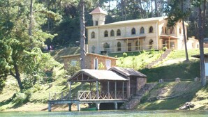 A large stone building with a tower, a dock, and a small covered structure. - Le Chateau du Lac (Mantasoa)