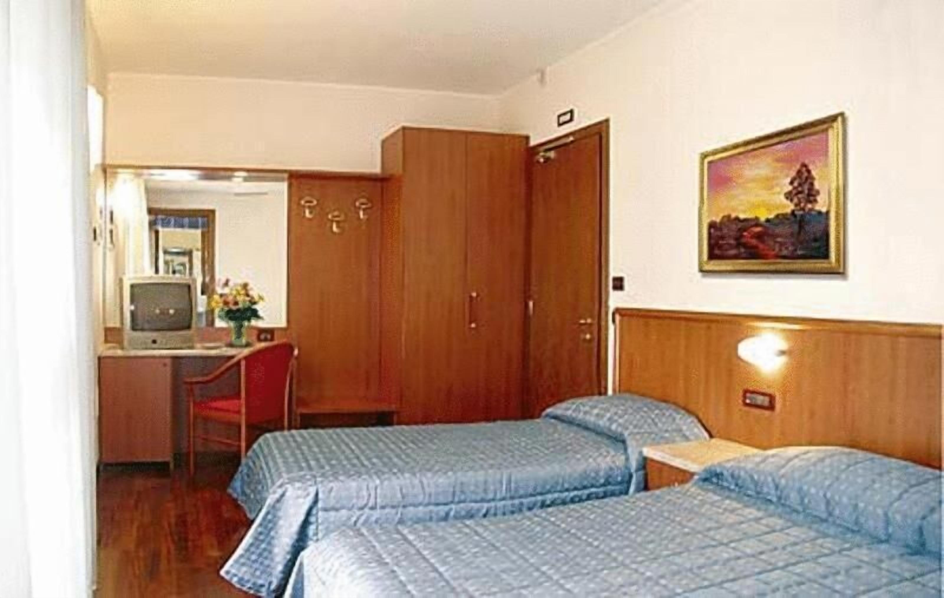 Una habitación con dos camas, un escritorio con computadora, una silla y un cuadro en la pared.