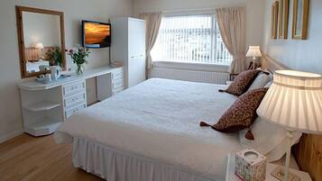 A neatly arranged bedroom with a bed, bedside lamps, a dresser, a television, and a window with curtains.