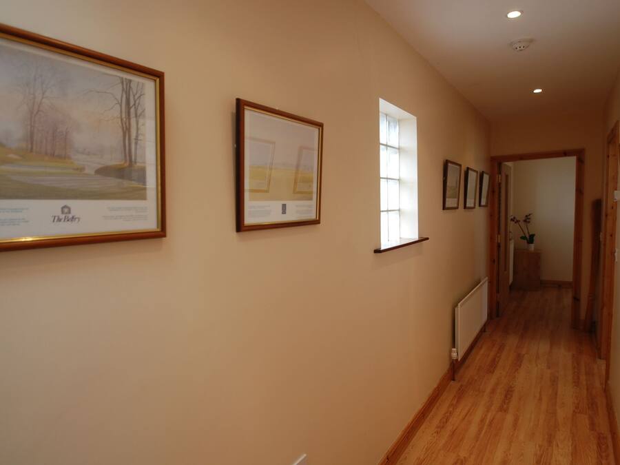 A hallway with framed pictures on the walls, a radiator, and wooden flooring.