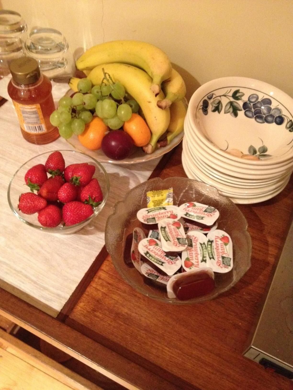 Una mesa con diversas frutas, como plátanos, uvas y fresas, y varios recipientes con alimentos.