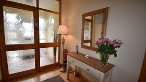 Una stanza con pavimento in legno, un tavolino consolle in legno, un vaso con fiori, una lampada e porte in vetro satinato.