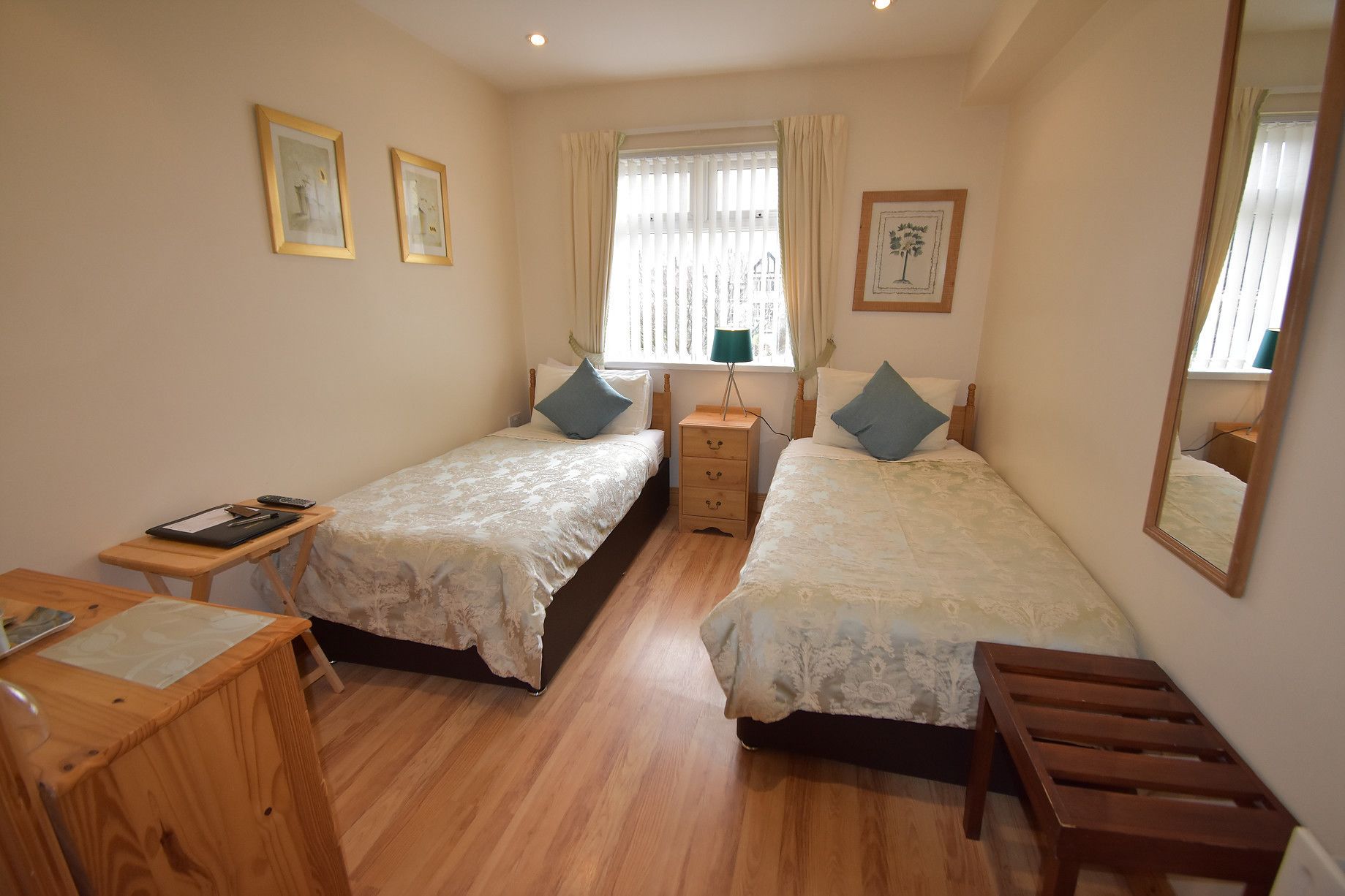 A bedroom with two single beds, a wooden desk, a nightstand, and a window with curtains.
