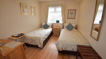 A bedroom with two single beds, a wooden desk, a nightstand, and a window with curtains.