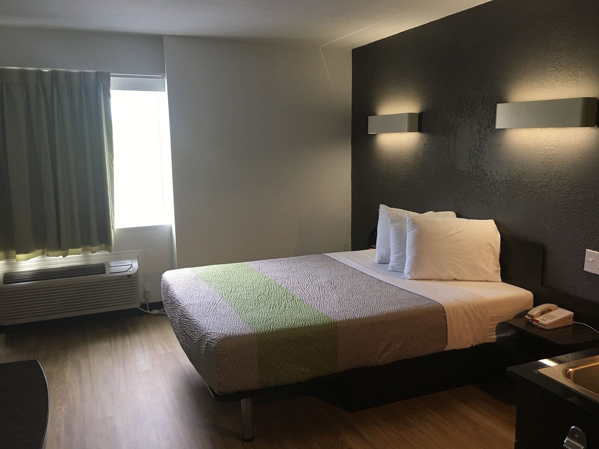 A hotel room with a bed, bedside table, and a window with curtains.