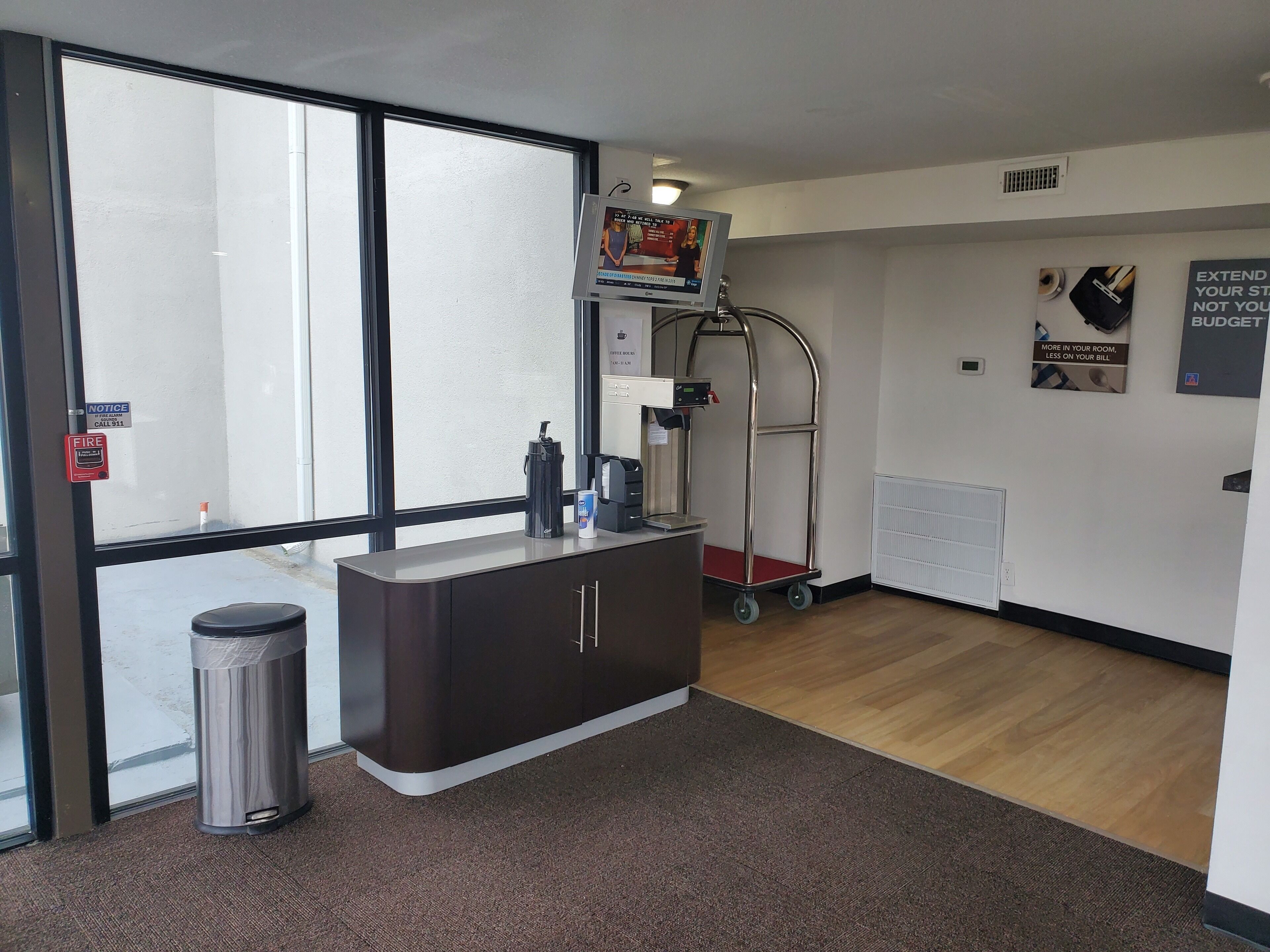 Un hall d’hôtel moderne comprenant un comptoir d’accueil, une machine à café, une poubelle et un chariot.
