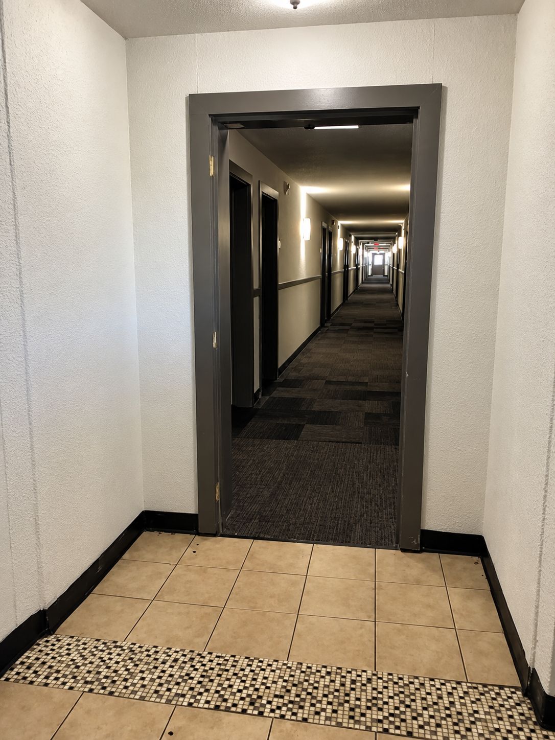 Un pasillo de hotel con pisos alfombrados, un borde de azulejos estampados y puertas que dan a las habitaciones.