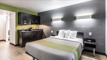 A modern hotel room with a bed, bedside table, and a kitchenette.