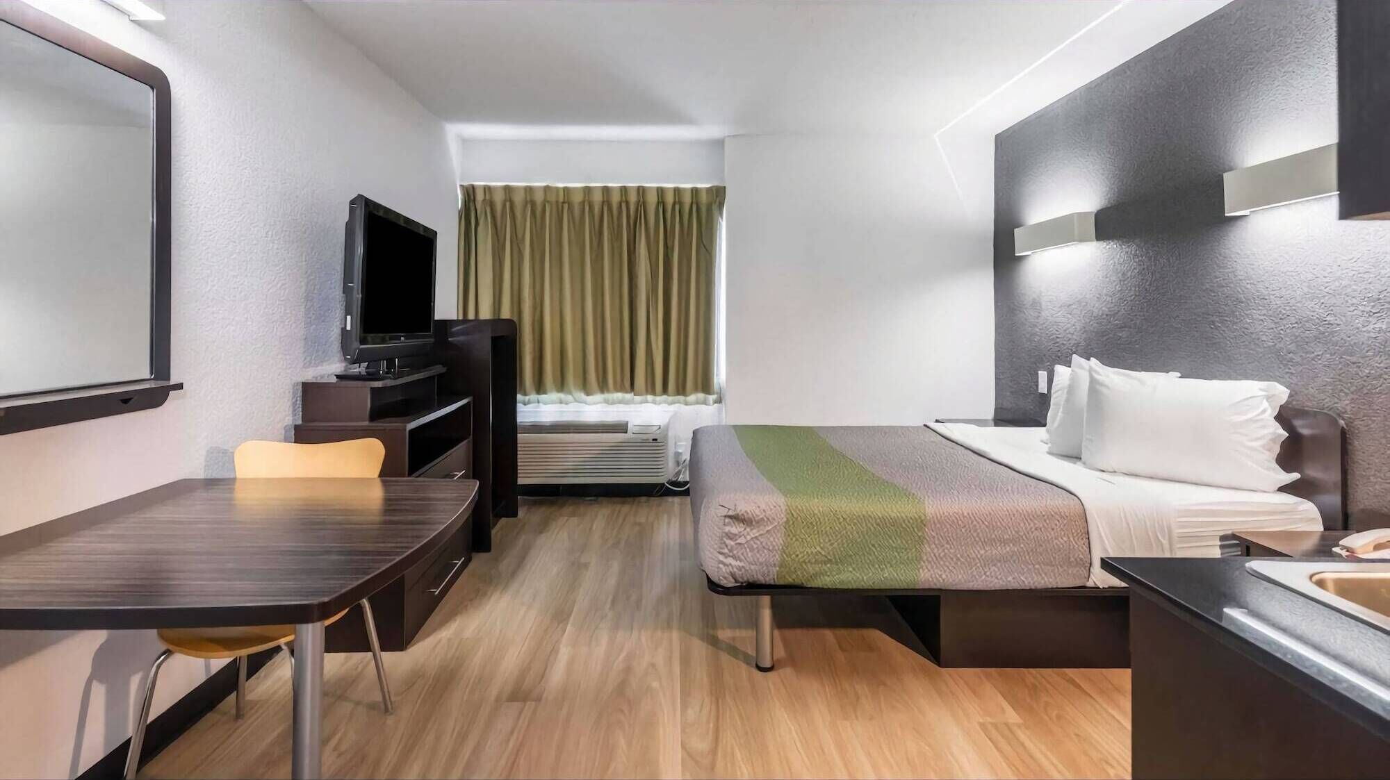 A hotel room with a bed, a desk, a TV, and a window with curtains.