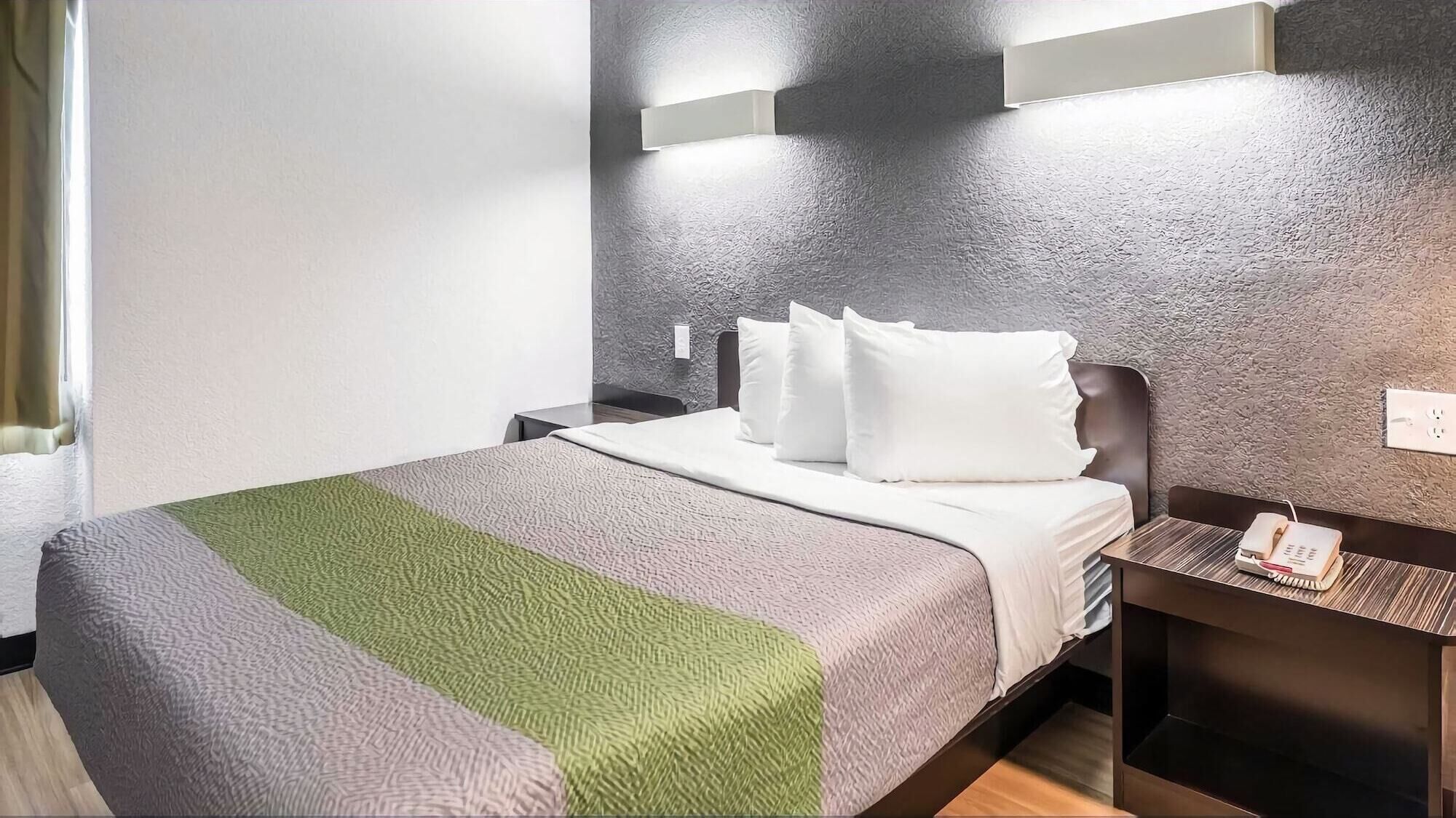 A hotel room with a bed, a nightstand, a wall-mounted light, and a textured wall.