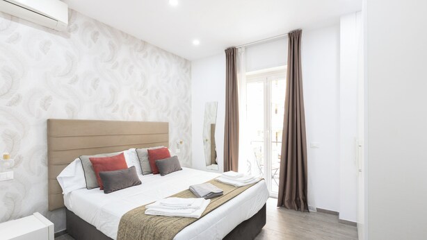 A modern hotel room with a large bed, a bedside table, and a view of the outside.