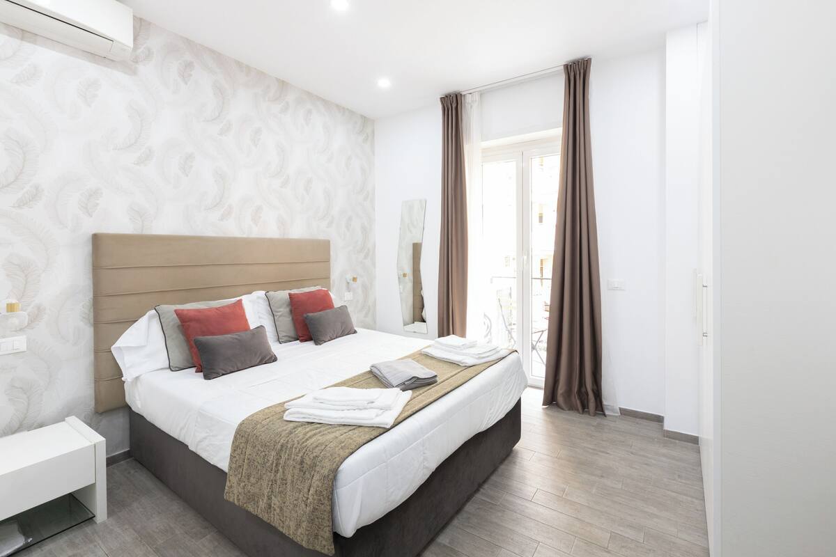 A modern hotel room with a large bed, a bedside table, and a view of the outside.