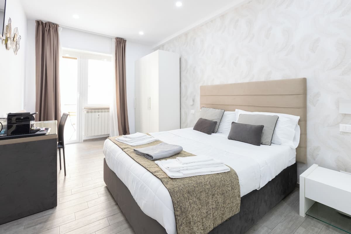 A modern hotel room with a large bed, a desk, and a view of the outdoors.