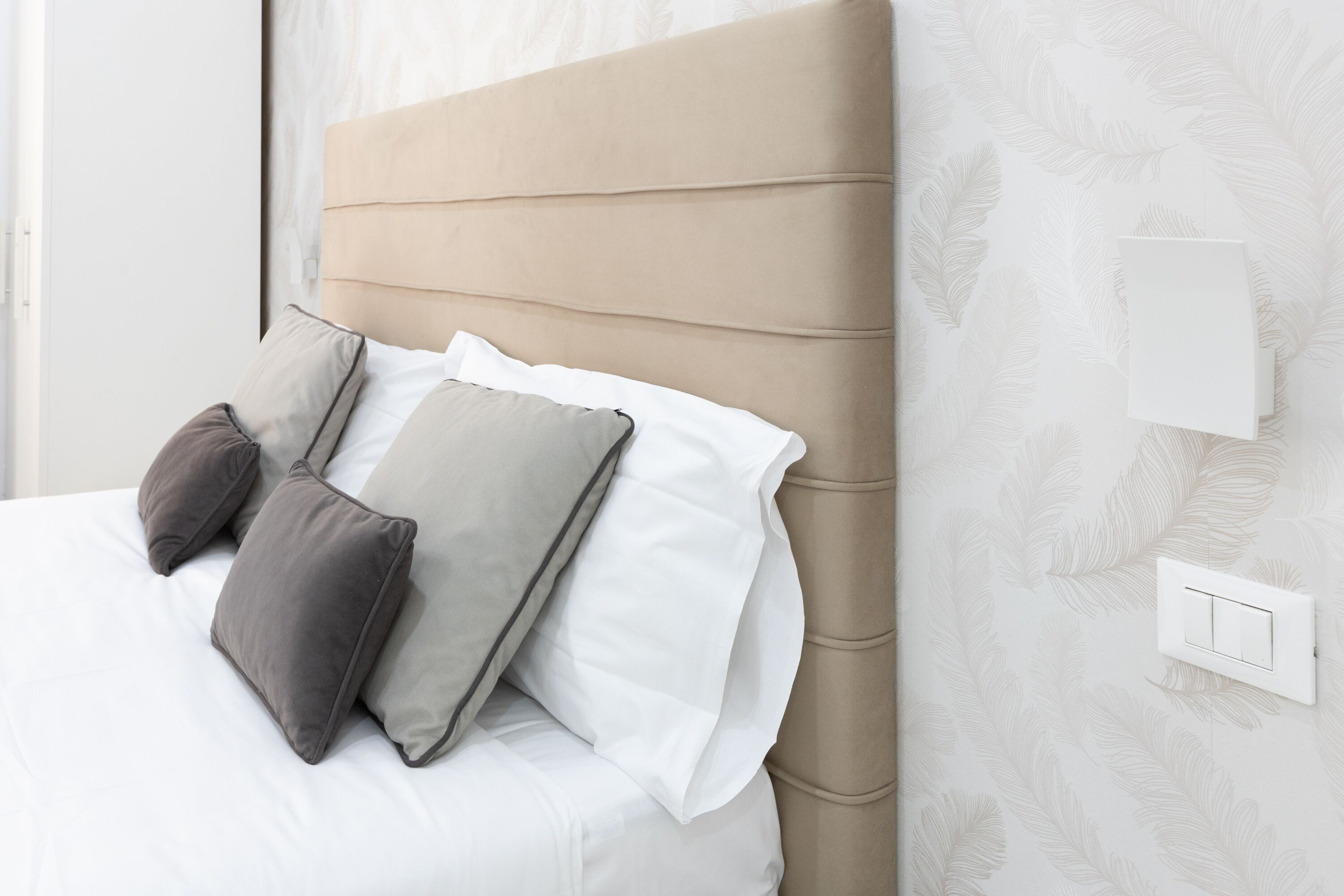 A bed with a beige headboard, white bedding, and two pillows.