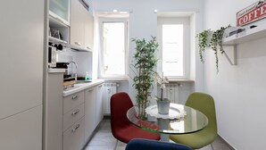 A compact kitchen with white cabinets, a red chair, a glass table, and a potted plant.