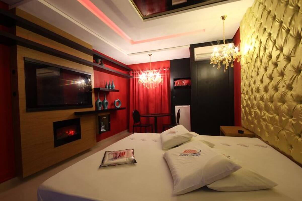 Une chambre d’hôtel moderne avec un grand lit, un téléviseur fixé au mur, un minibar et un rideau rouge.